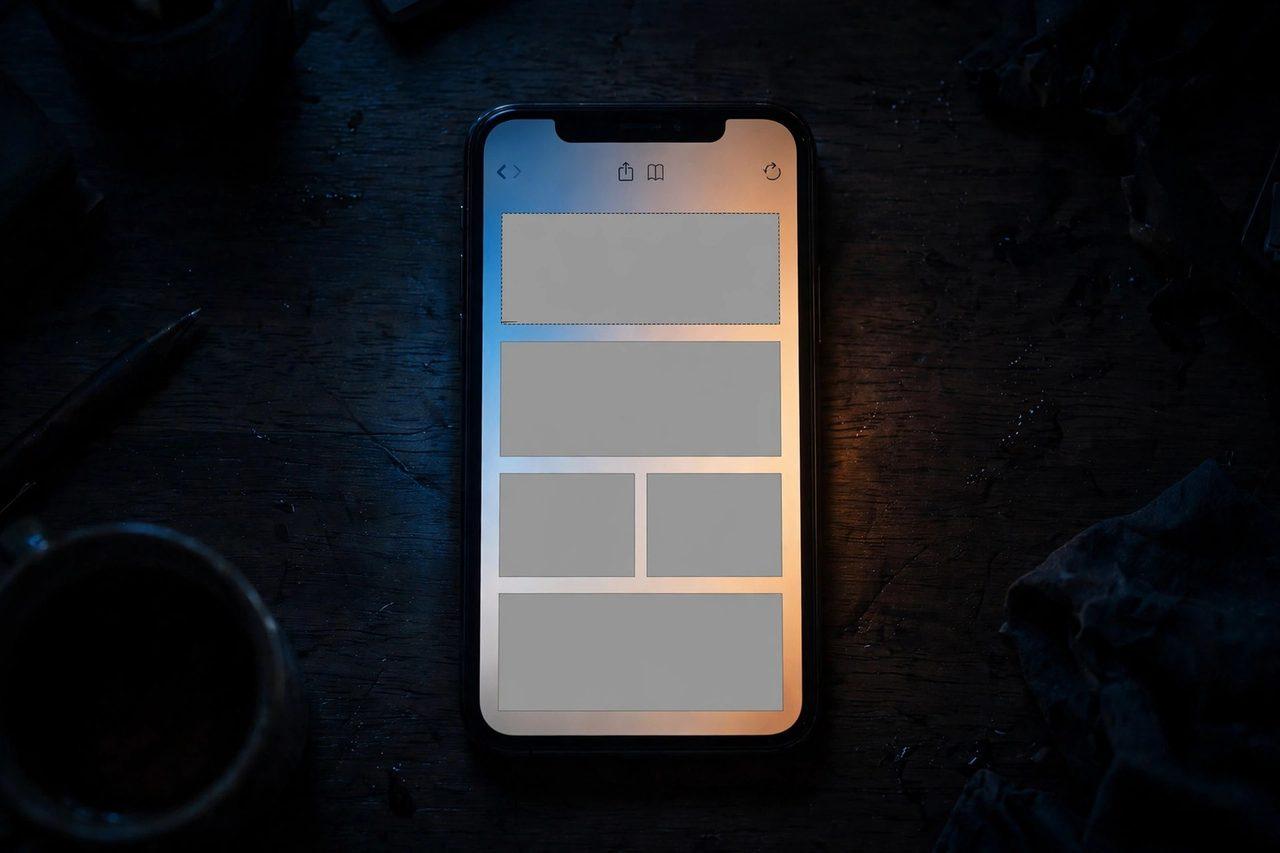 An iPhone glowing amber and blue in a dark room, Safari open on a news article with empty blocked ad slots marked by a red gate