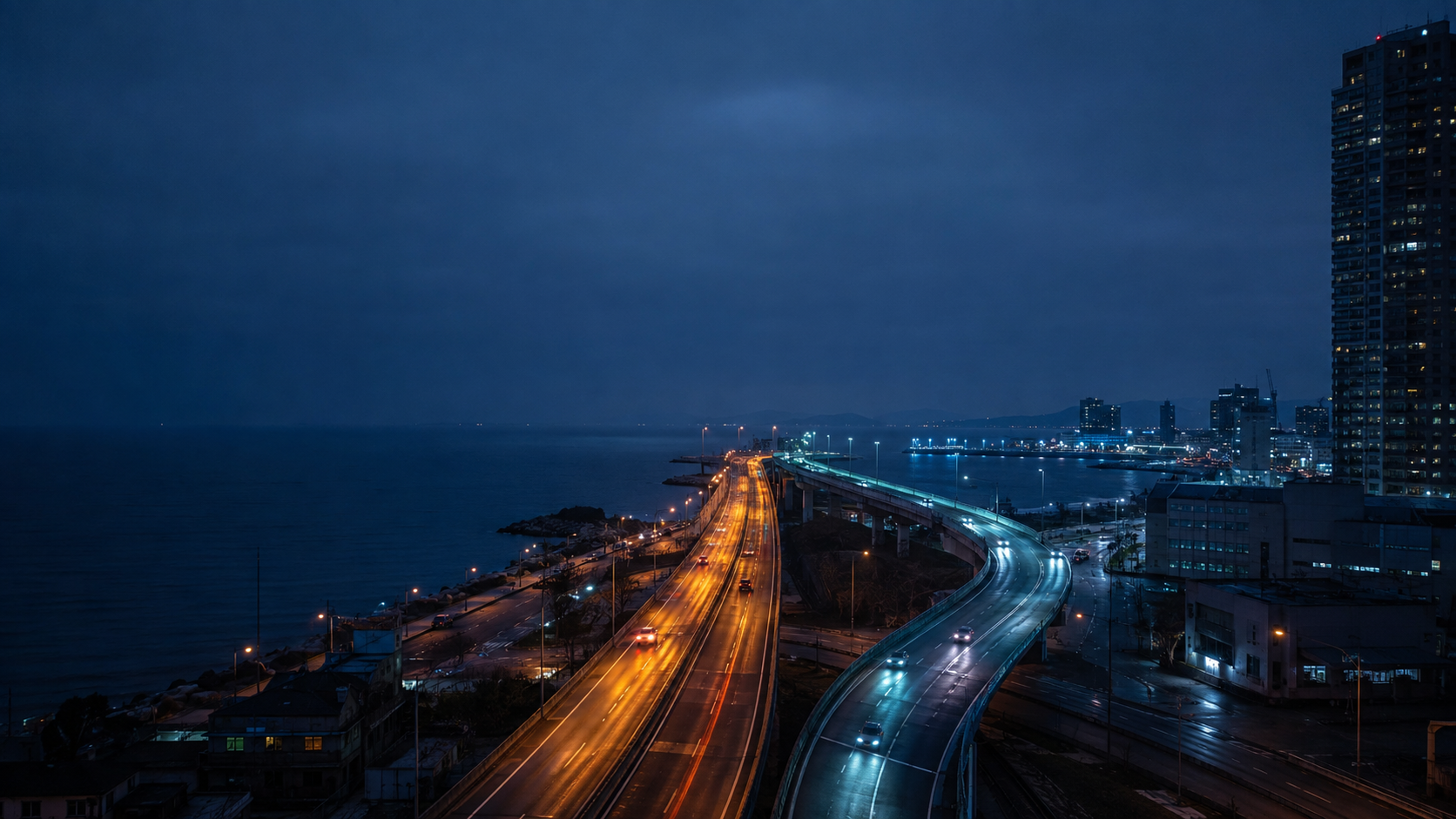 A coastal interchange at blue hour with amber and cyan roads carrying attention in different directions.